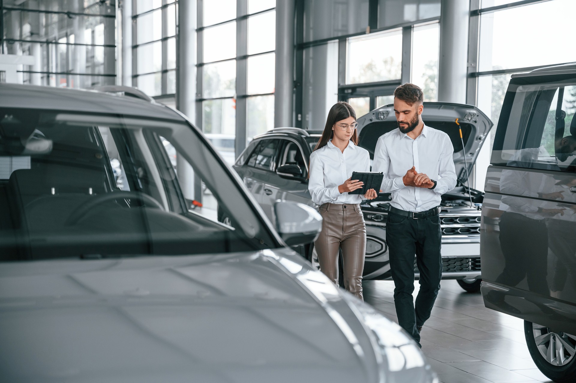 Walking forward and talking. Man with woman in white clothes are in the car dealership together