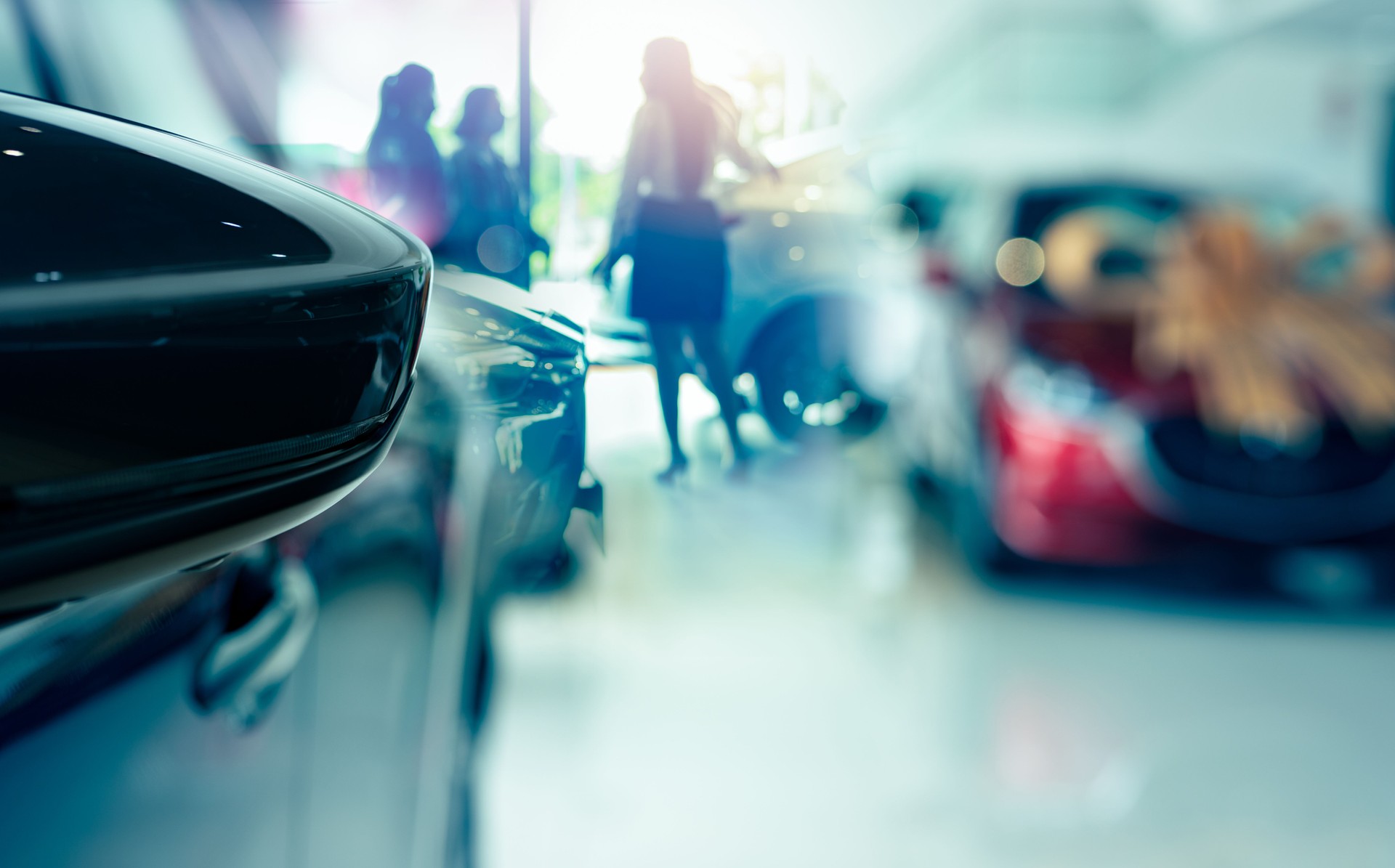 Selective side mirror car on blur saleswoman and customer in modern luxury showroom. Car dealership office concept. Dealer agent business. Automobile leasing service. Dealer company. New car purchase.